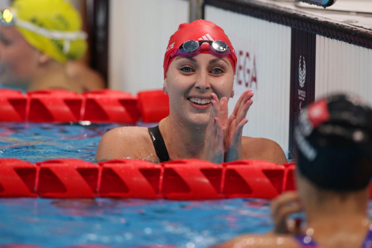 A female Para swimmer claps her hands in the pool after finishing her race.