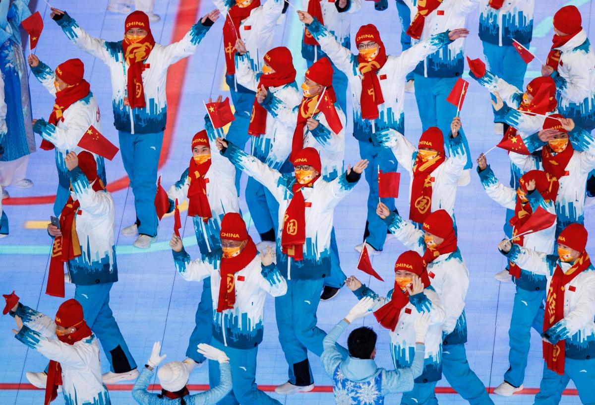 About 20 people march in the main stadium of the Beijing 2022 Games while waving small Chinese flags.