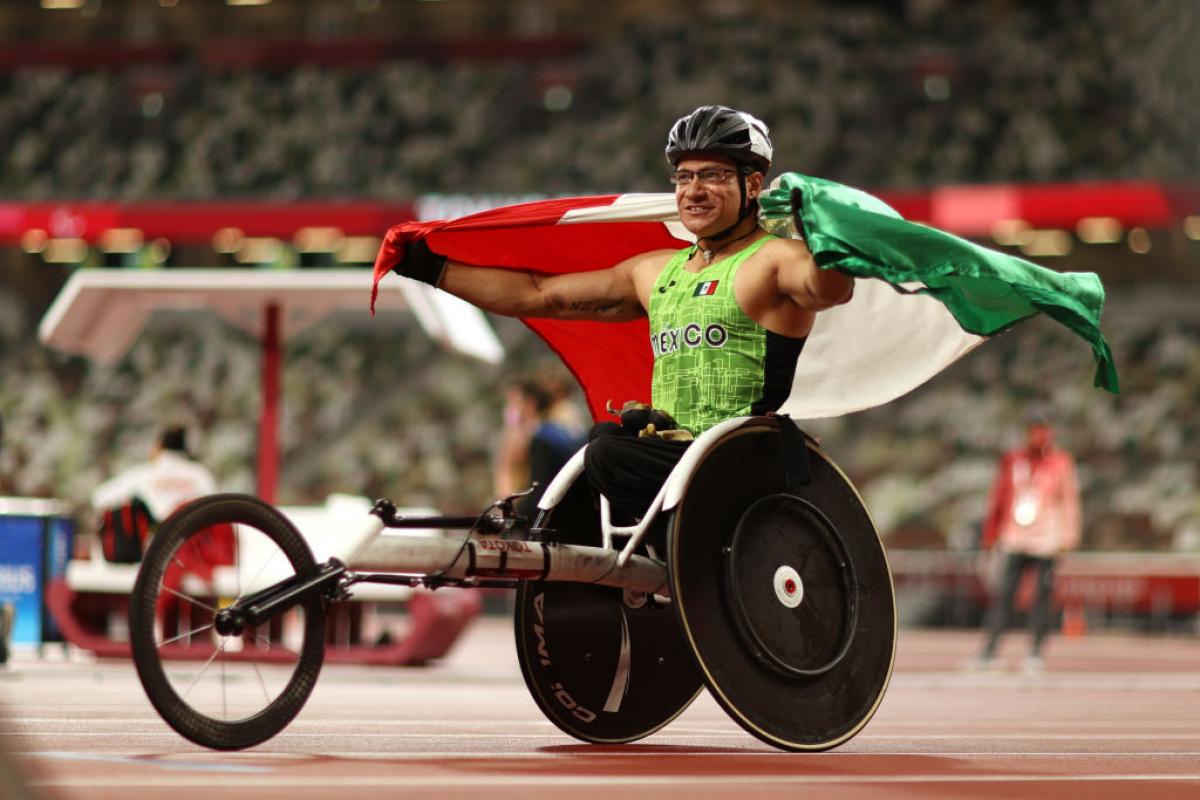 A male wheelchair racer with the Mexican flag at an athletics track