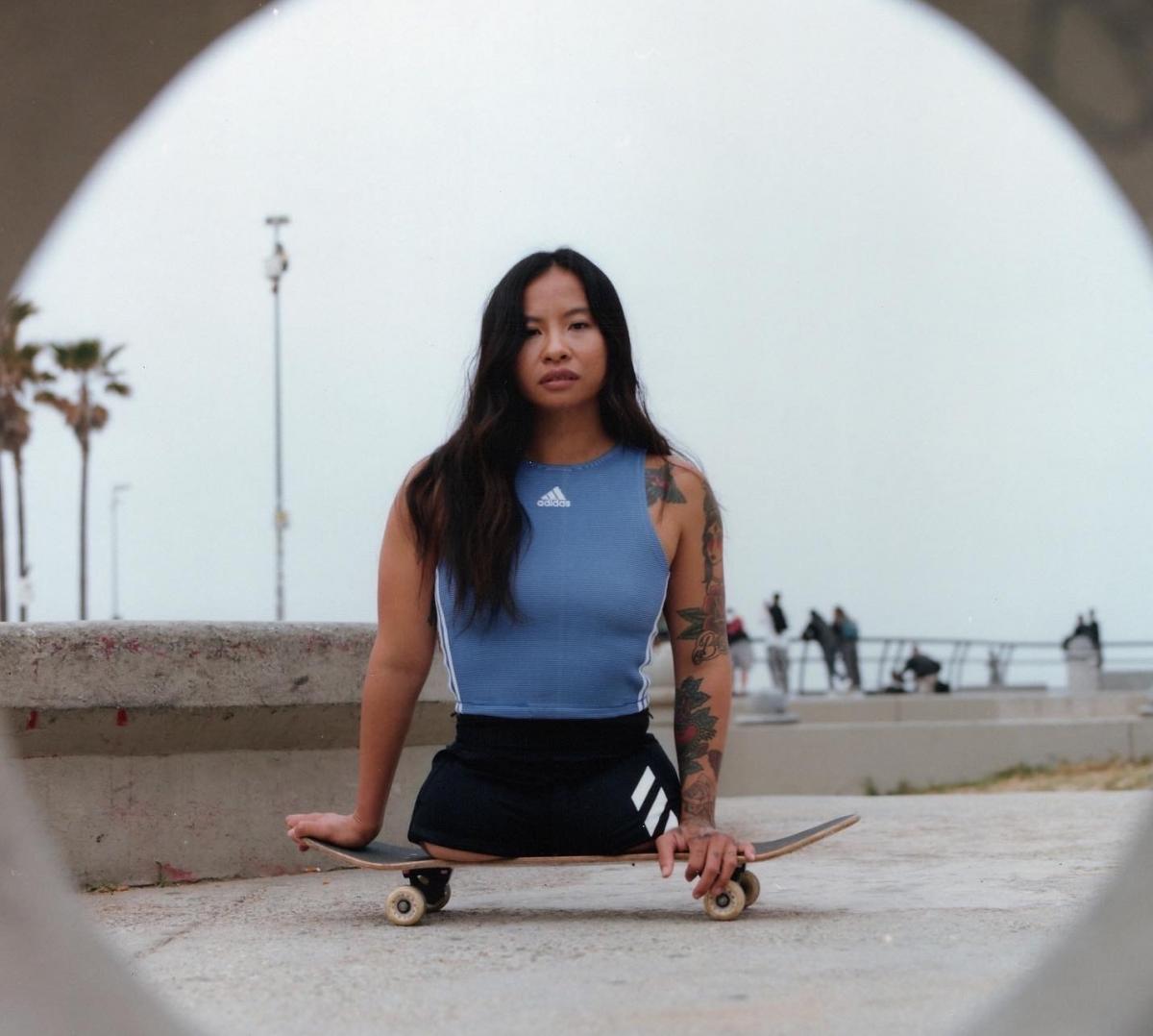 A young female without legs sits on a skateboard while wearing sports gear.