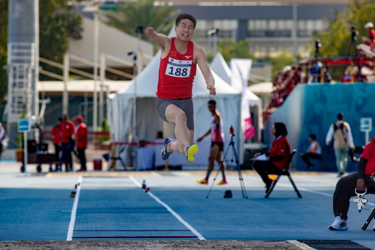 A one-armed man jumping in a long jump competition in a blue athletics track