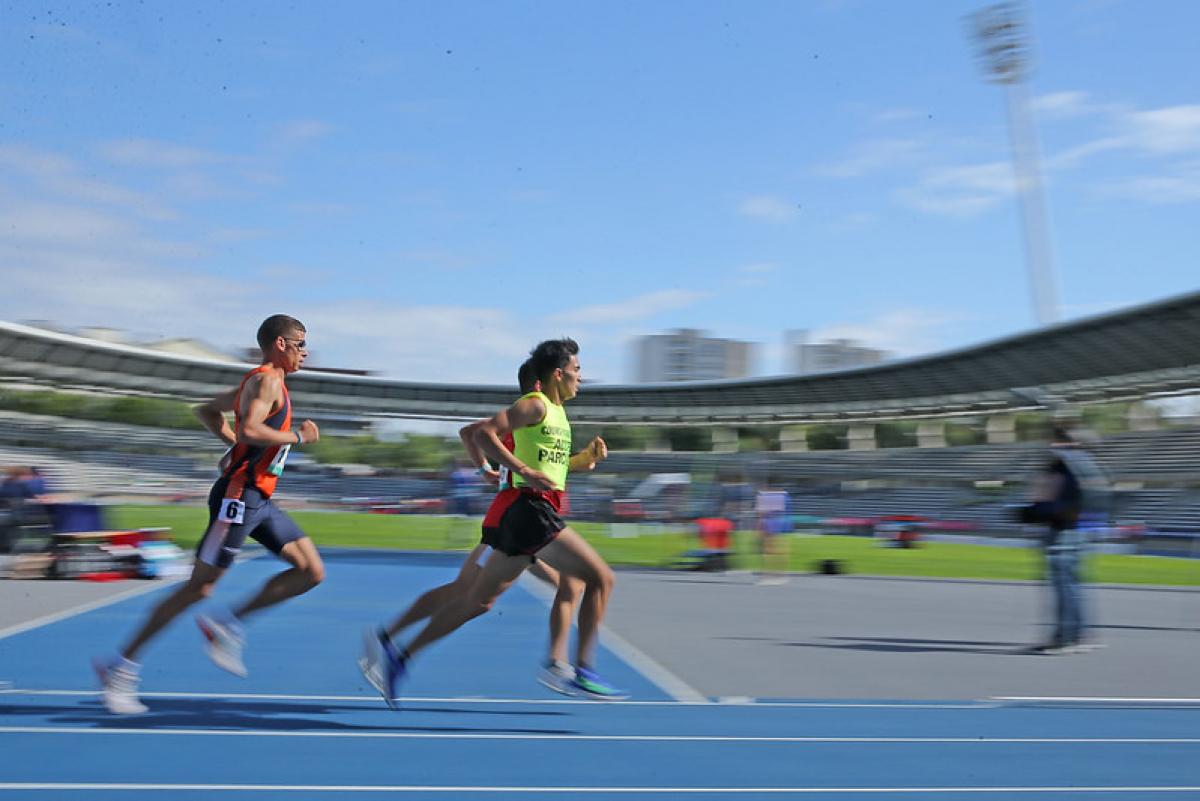 Three men running in a blue athletics track during a Para athletics event at Charlety Stadium in Paris