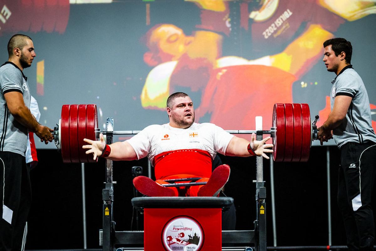 A male powerlifter in a bench press with two men standing next to him