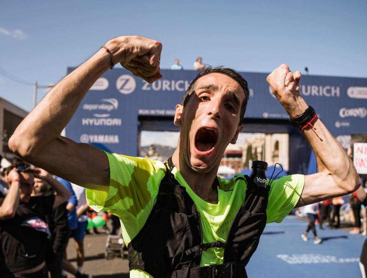 A male runner with cerebral palsy raises his hands in the air at the finish line of the Barcelona Marathon.