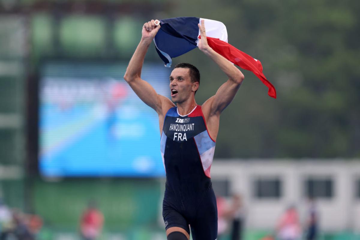 A male Para triathlete reacts to his victory at the Tokyo 2020 Paralympic Games by waving the French flag in the air.