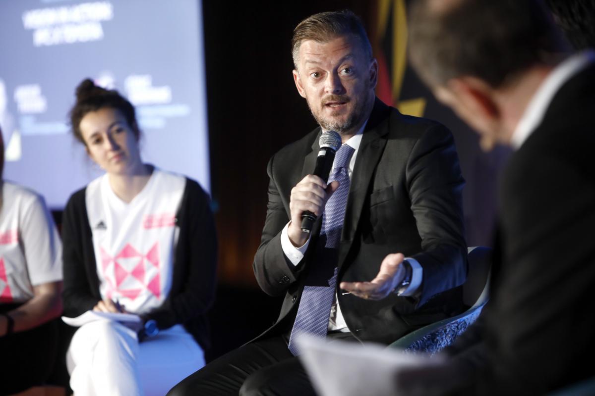A man in a suit speaks into a microphone during a discussion session at Global Sport Week in Paris. 