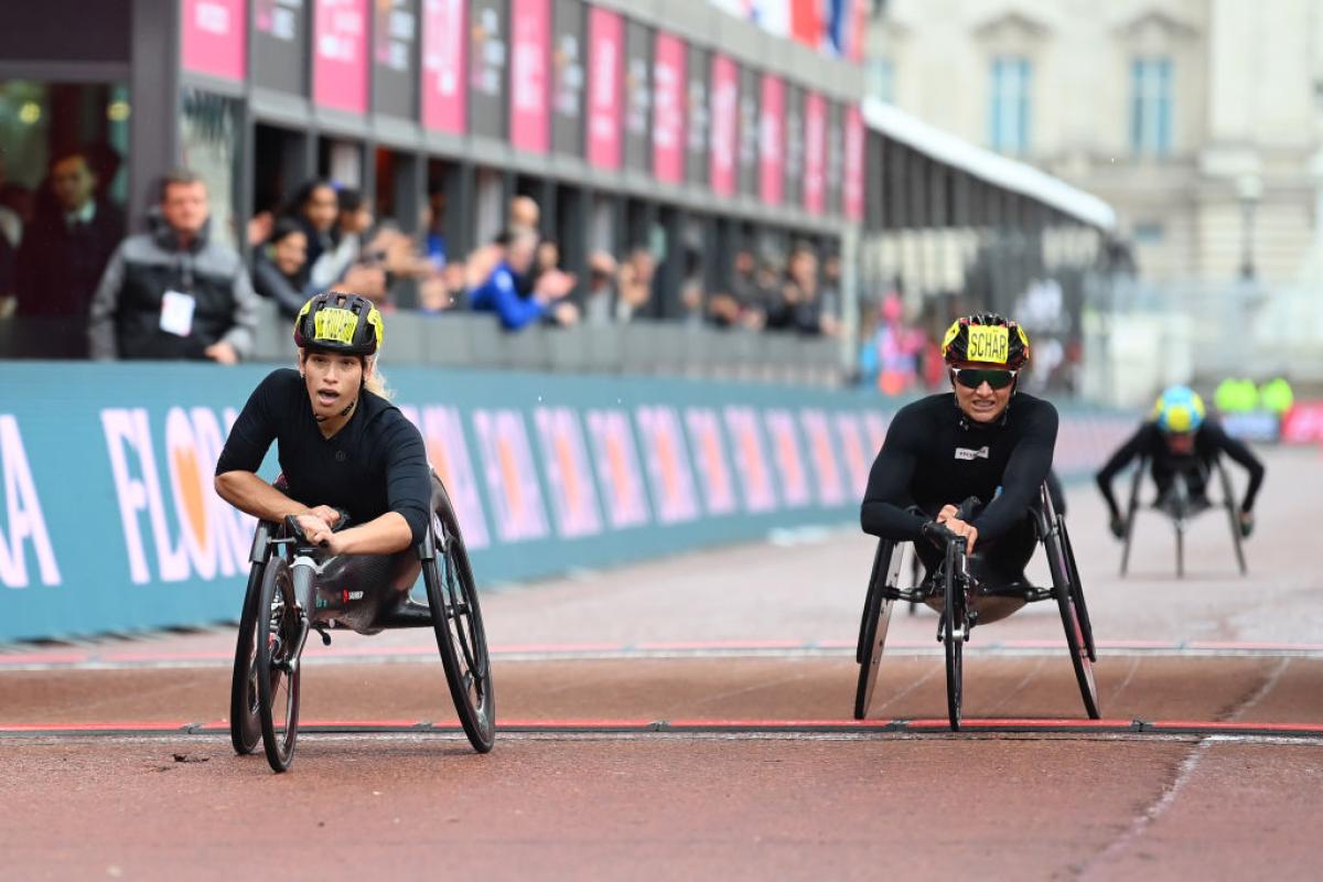 A female wheelchair racer crossing the finish line ahead of another racer in a street marathon