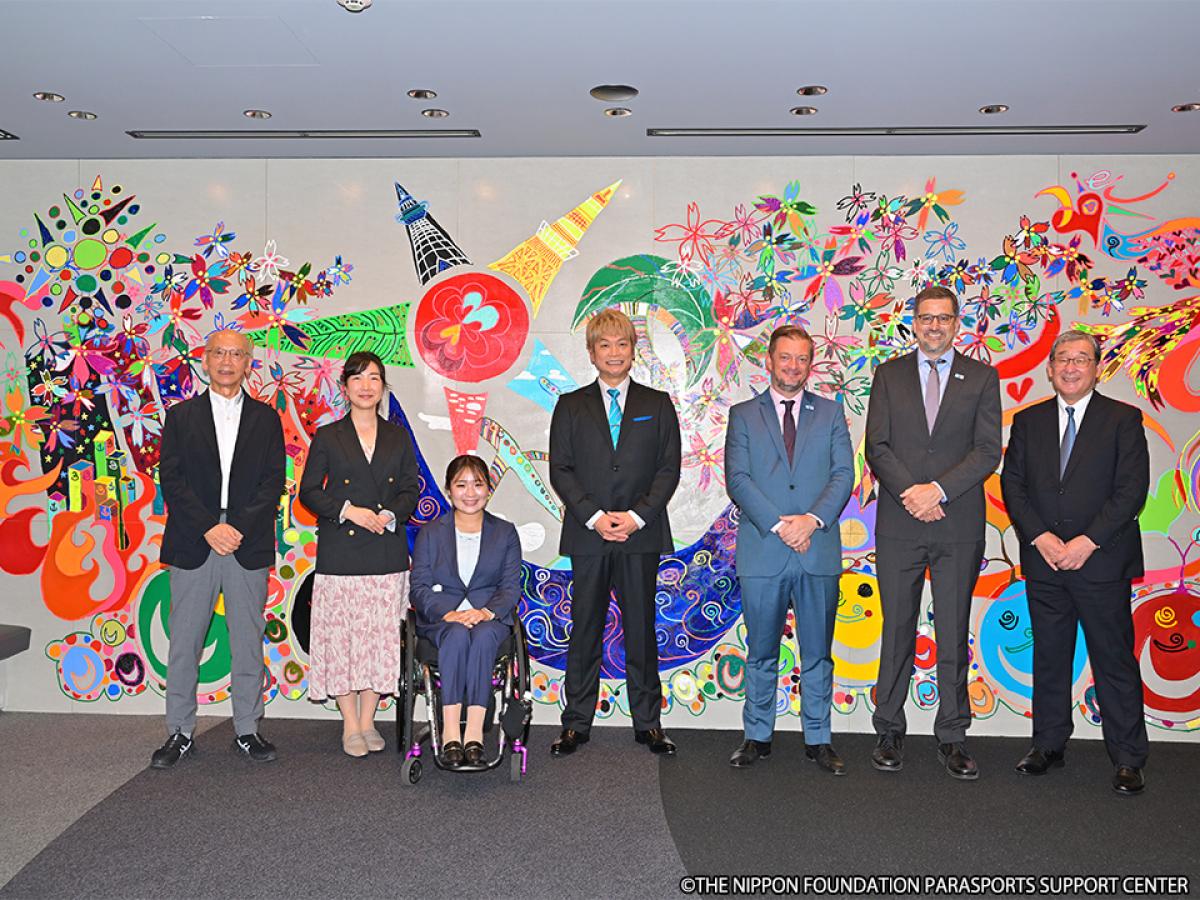 Seven people pose for a photograph in front of an artwork.