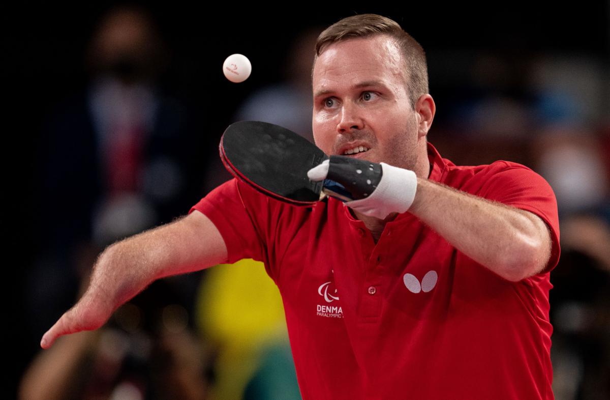 A male athlete wearing a red T-shirt plays table tennis