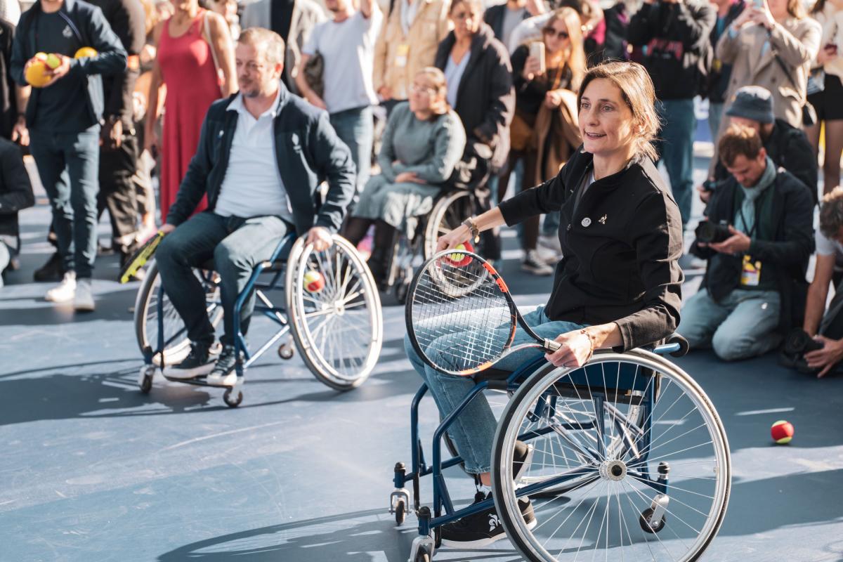 A woman and a man on a wheelchair holding tennis racquet.