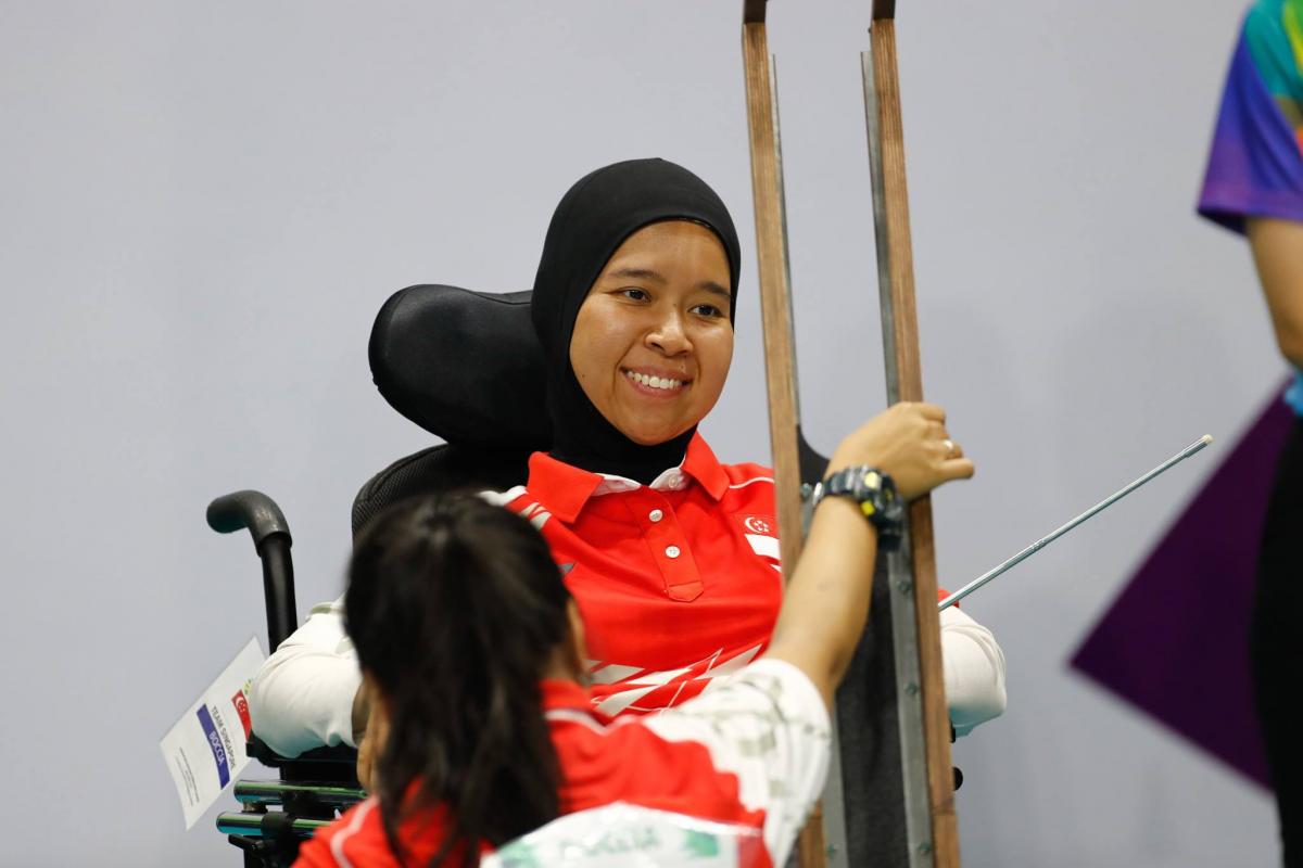A female boccia athlete looks at her boccia ramp, while her assistant holds it.