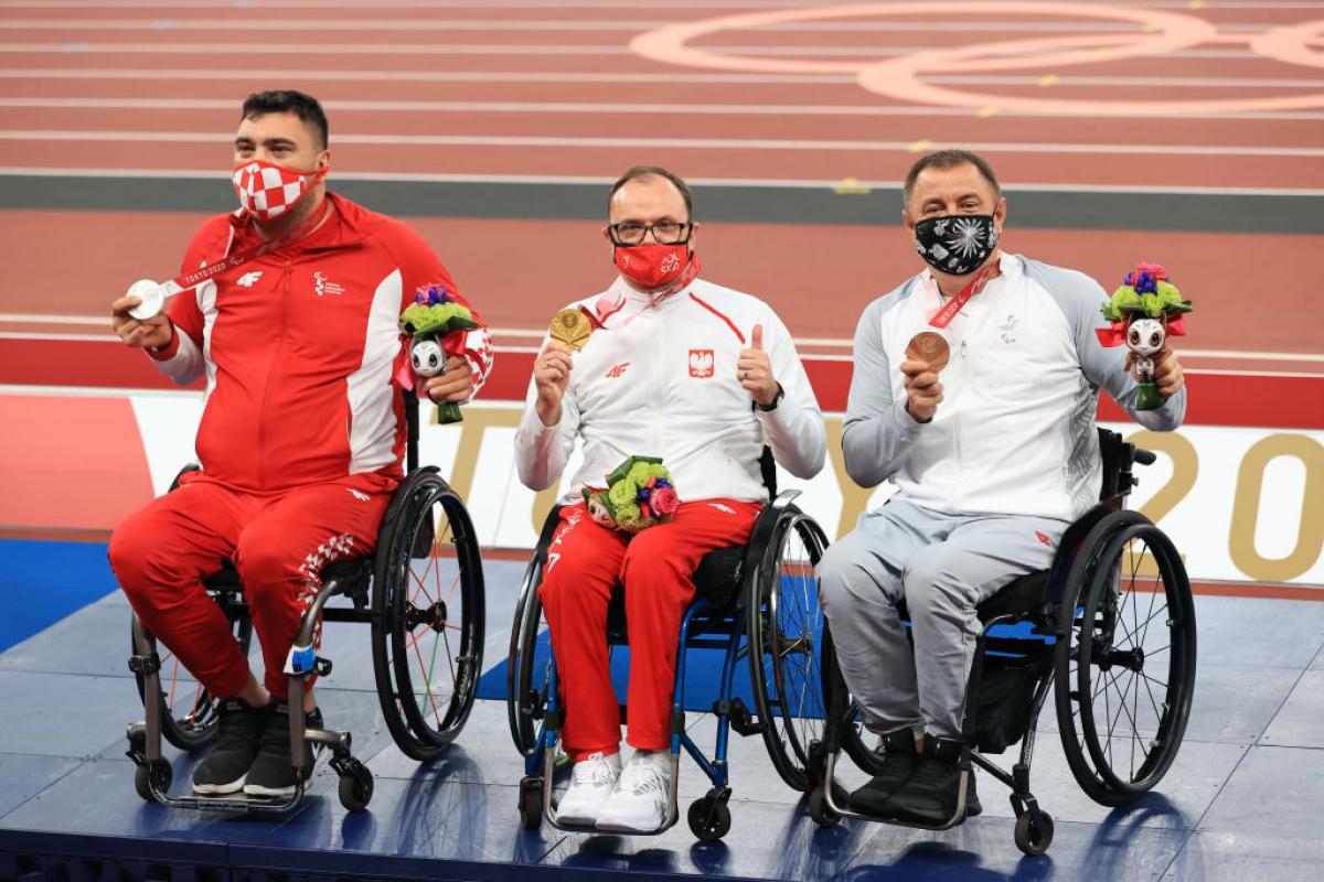 Three male athletes on wheelchairs posing for a photo with medals.