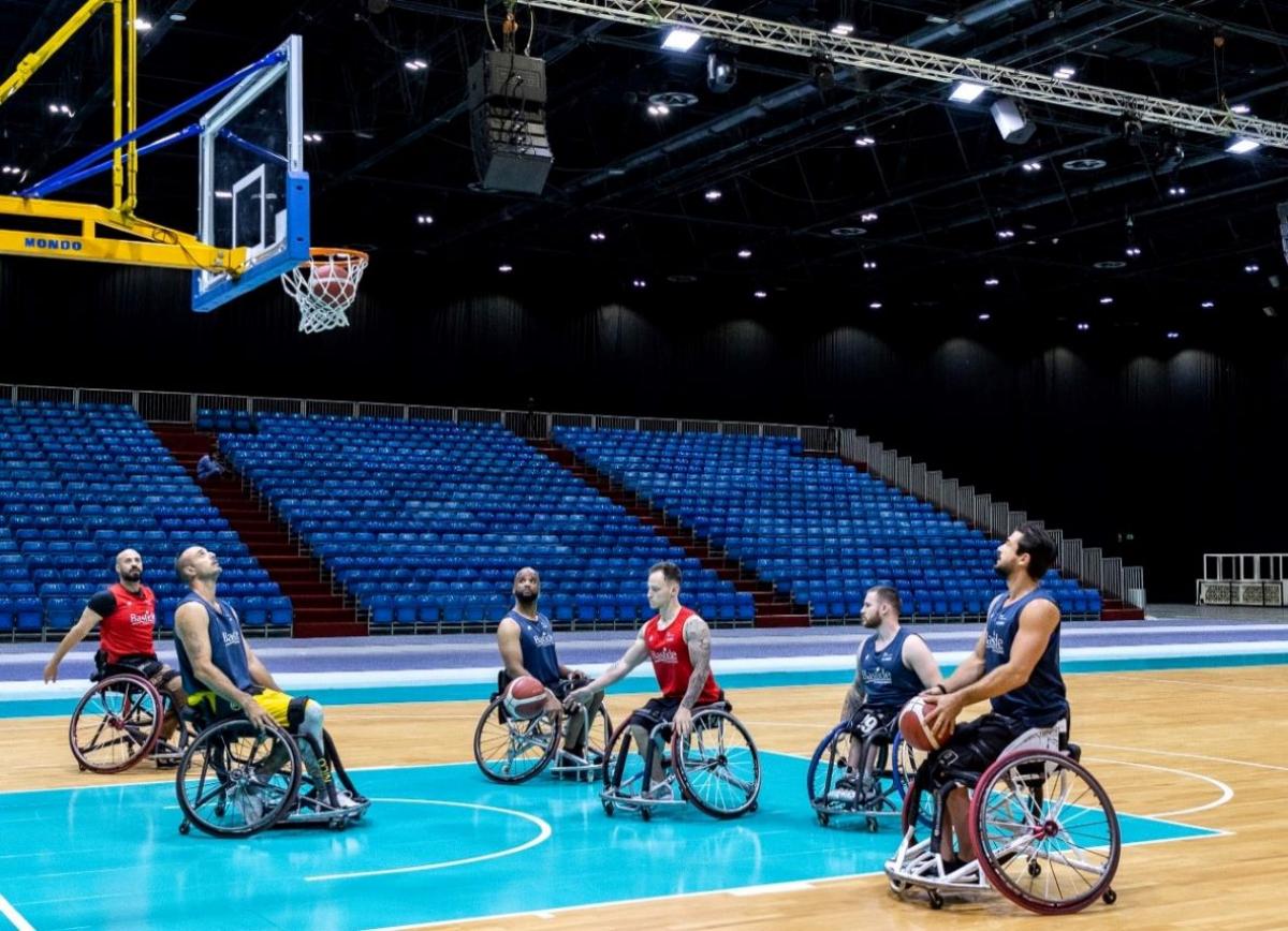 Six wheelchair basketball players train at an indoor hall.