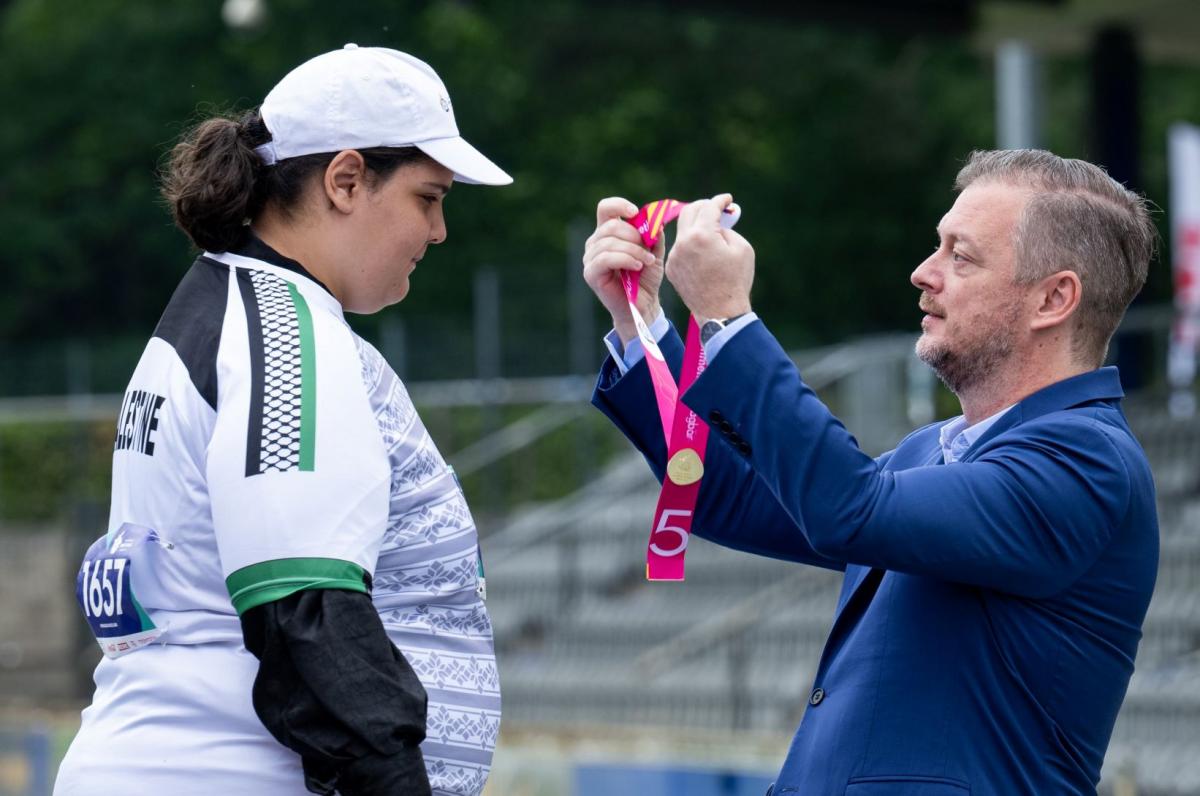 A man wearing a blue suit presents a medal to a female athlete.