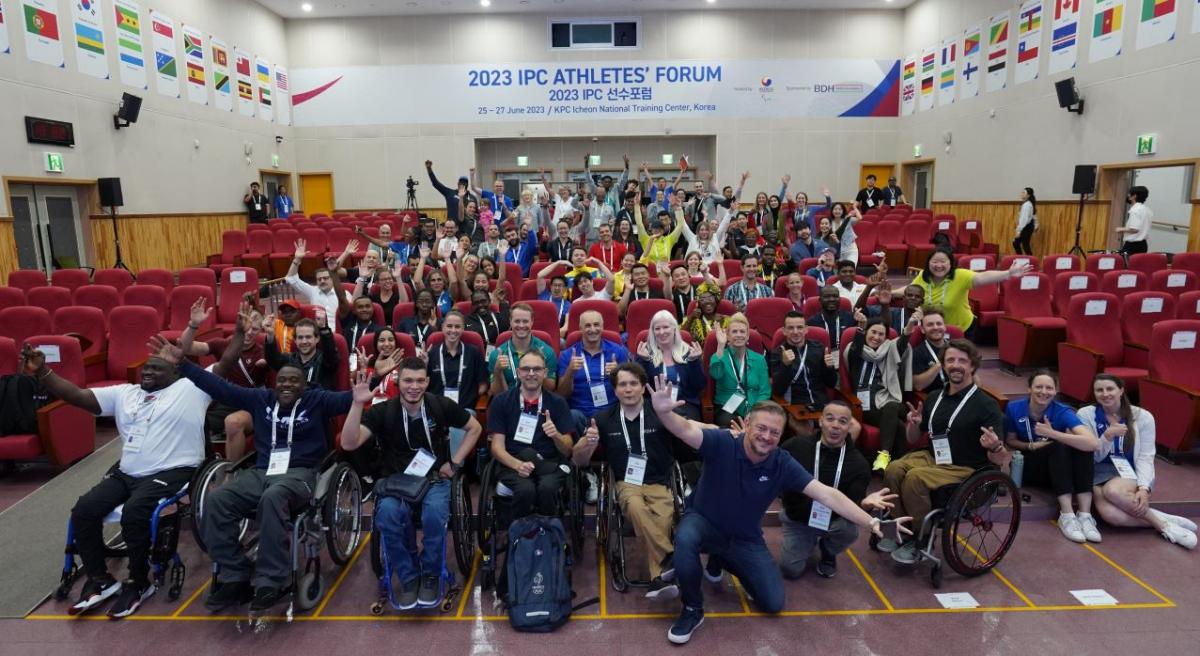 About 60 people pose for a photograph in an auditorium.