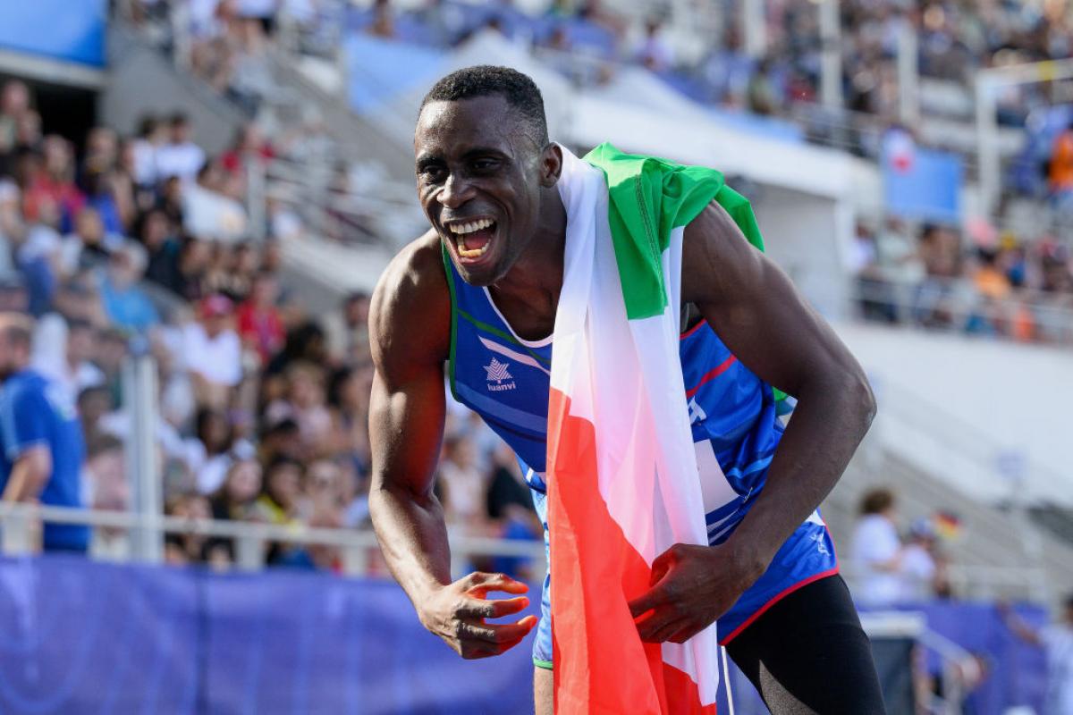 A man in athletics outfit celebrating with the Italian flag