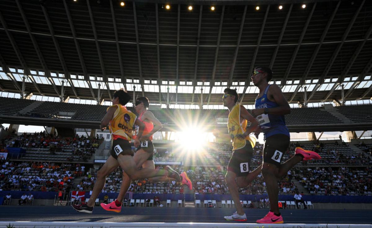 two vision impaired runners and their guides running on the track in front of spectators