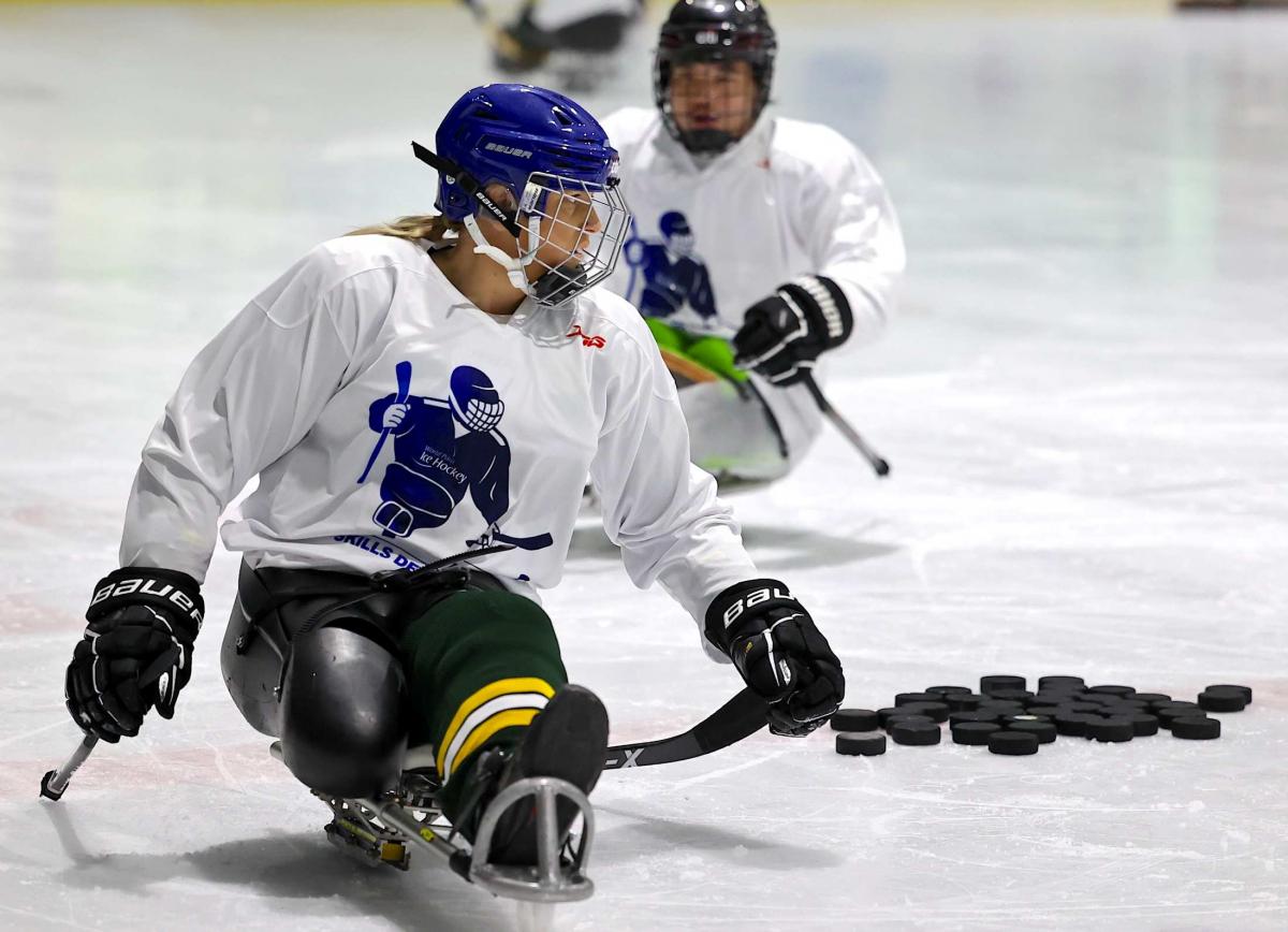 A female Para ice hockey player on an ice rink followed by a male player