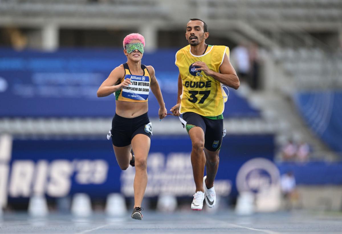 A female runner wearing green blindfolds competes with her guide runner