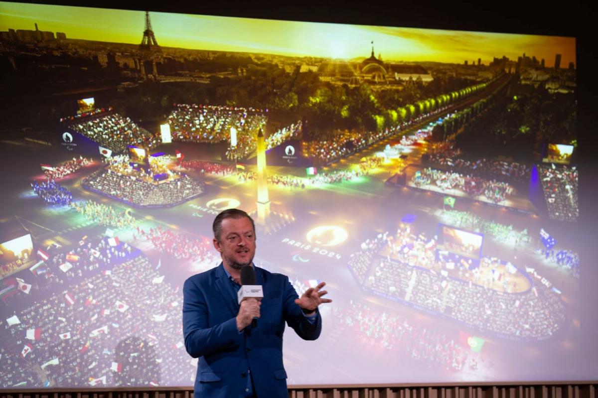 IPC President Andrew Parsons speak in front of a screen showing the Opening Ceremony of the Paris 2024 Paralympic Games