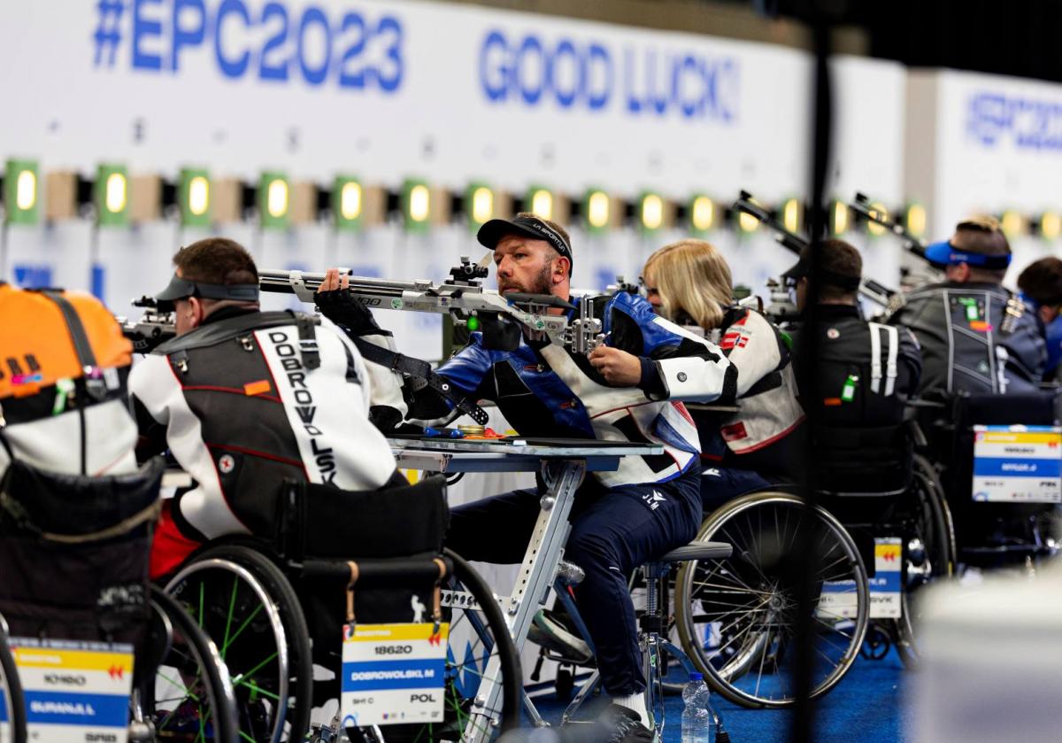 A group of five male and female rifle shooters in wheelchairs in a shooting range