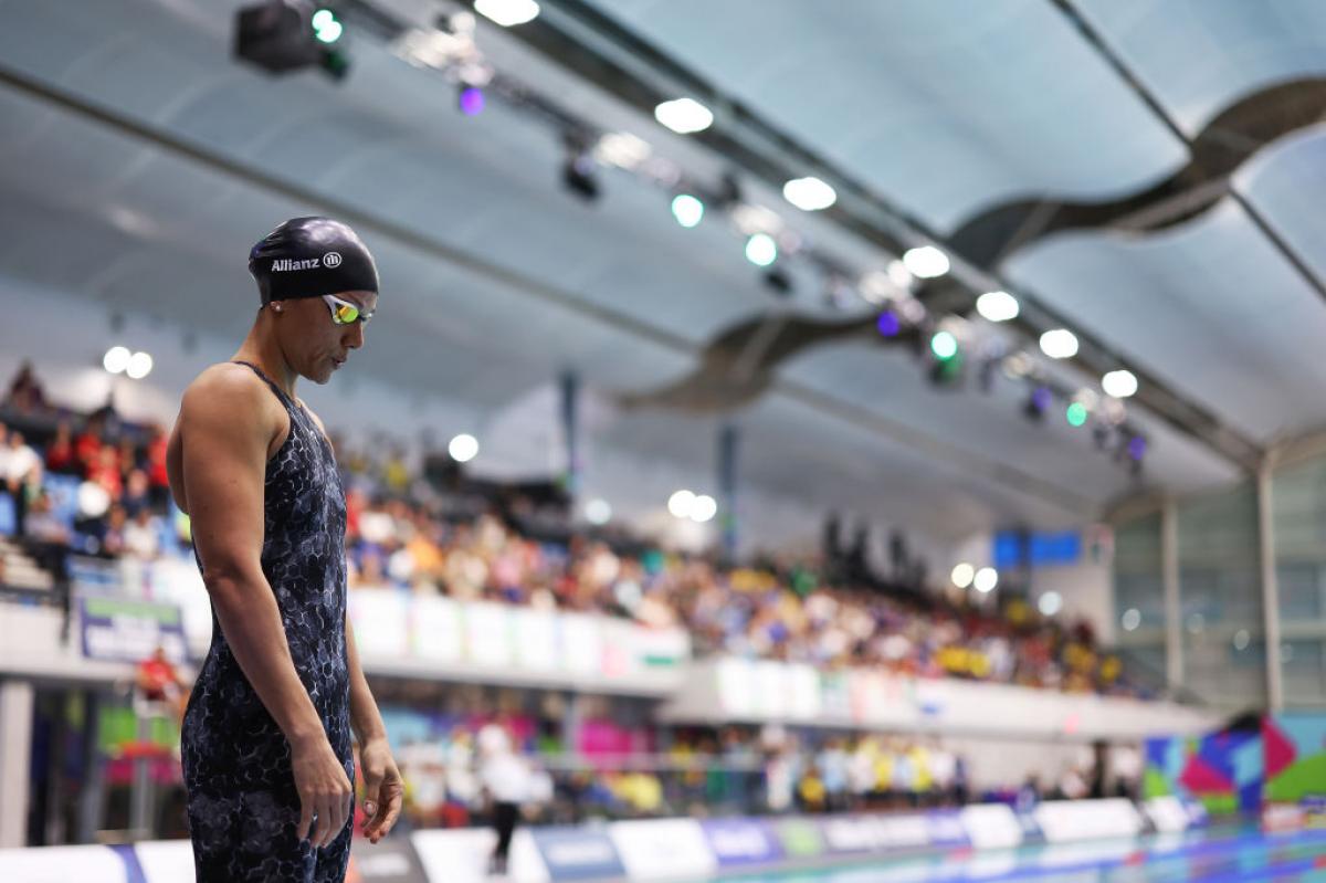 A female swimmer standing next to a pool in a crowded venue