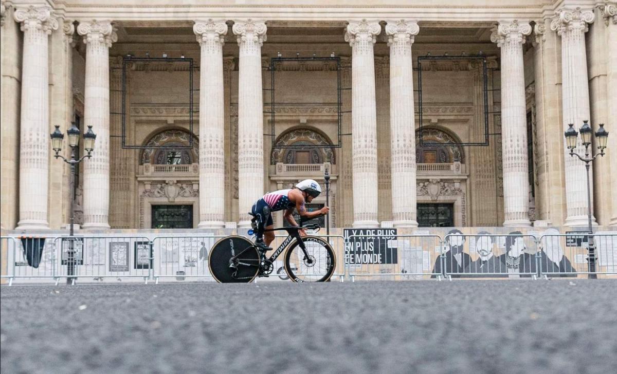 A Para triathlete on a bike cycles past a Parisian monument 