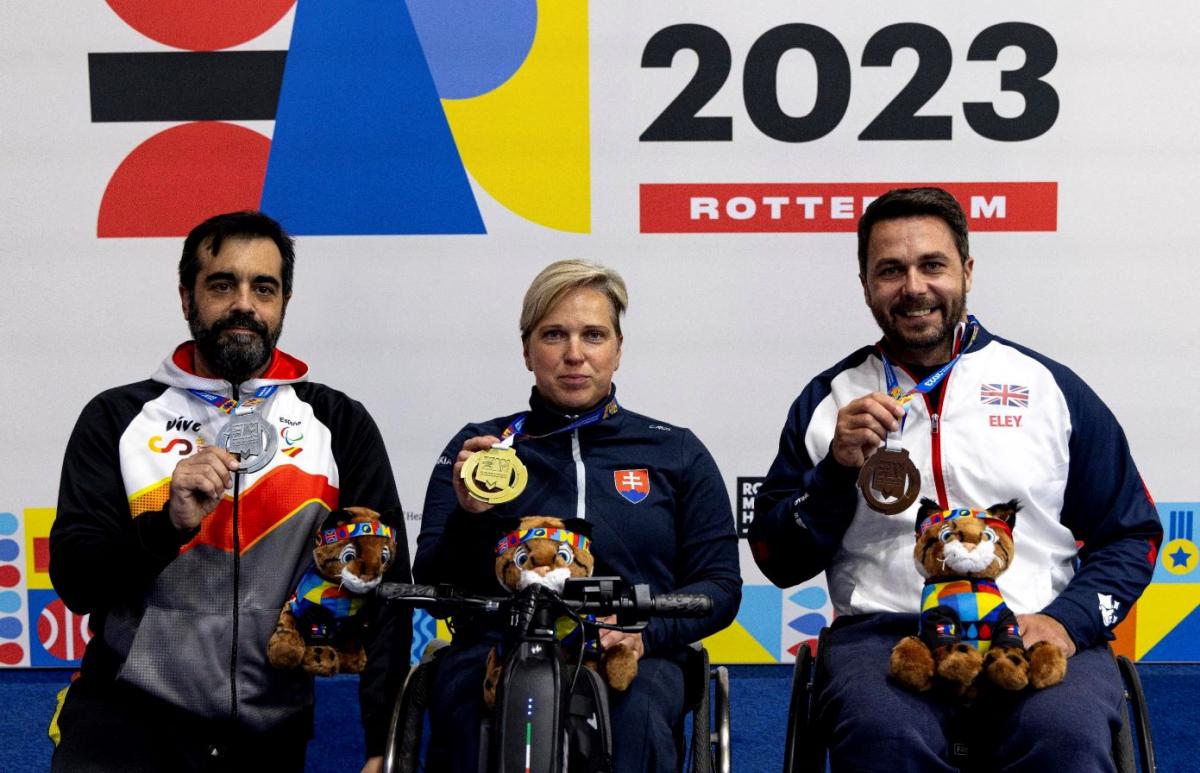 A woman in a wheelchair between two men on a podium