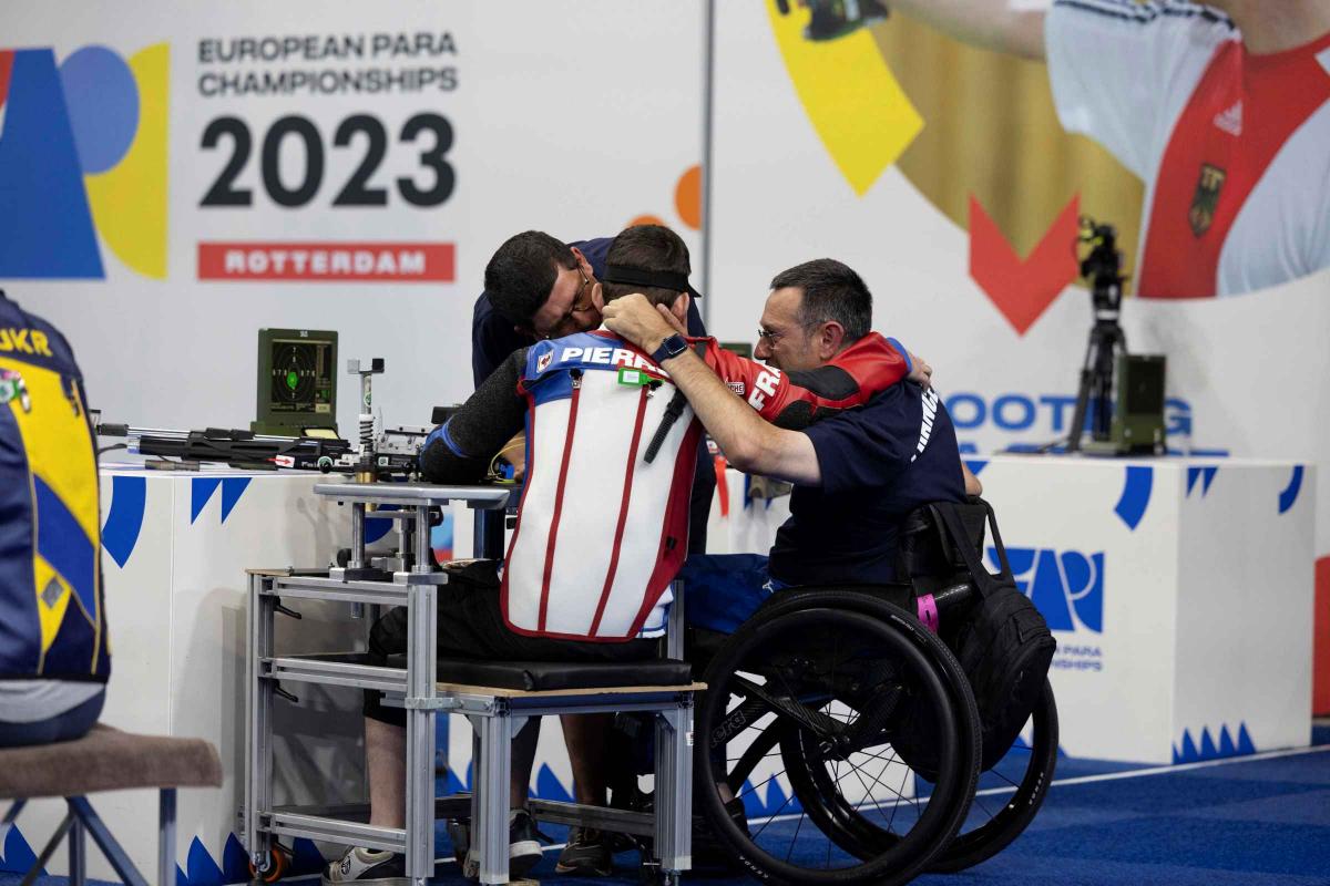 A man in a wheelchair chair hugging two other men