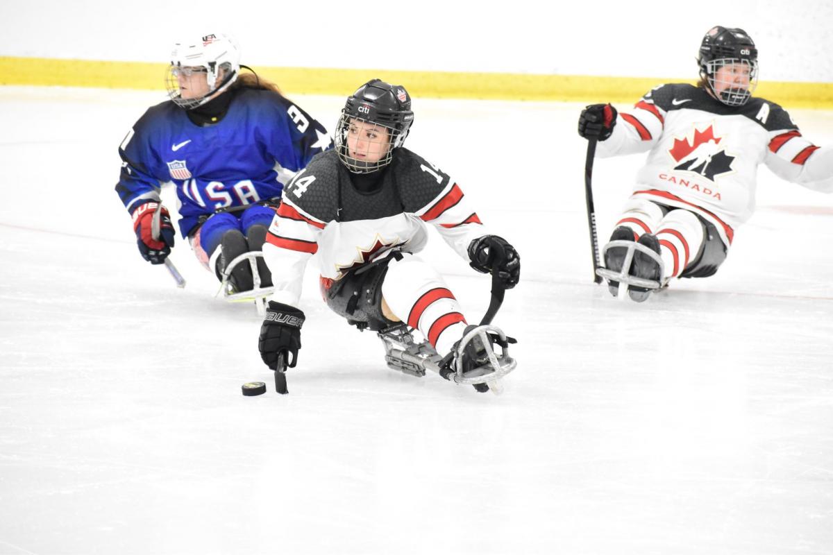 A Canadian female Para ice hockey player on ice followed by a USA player