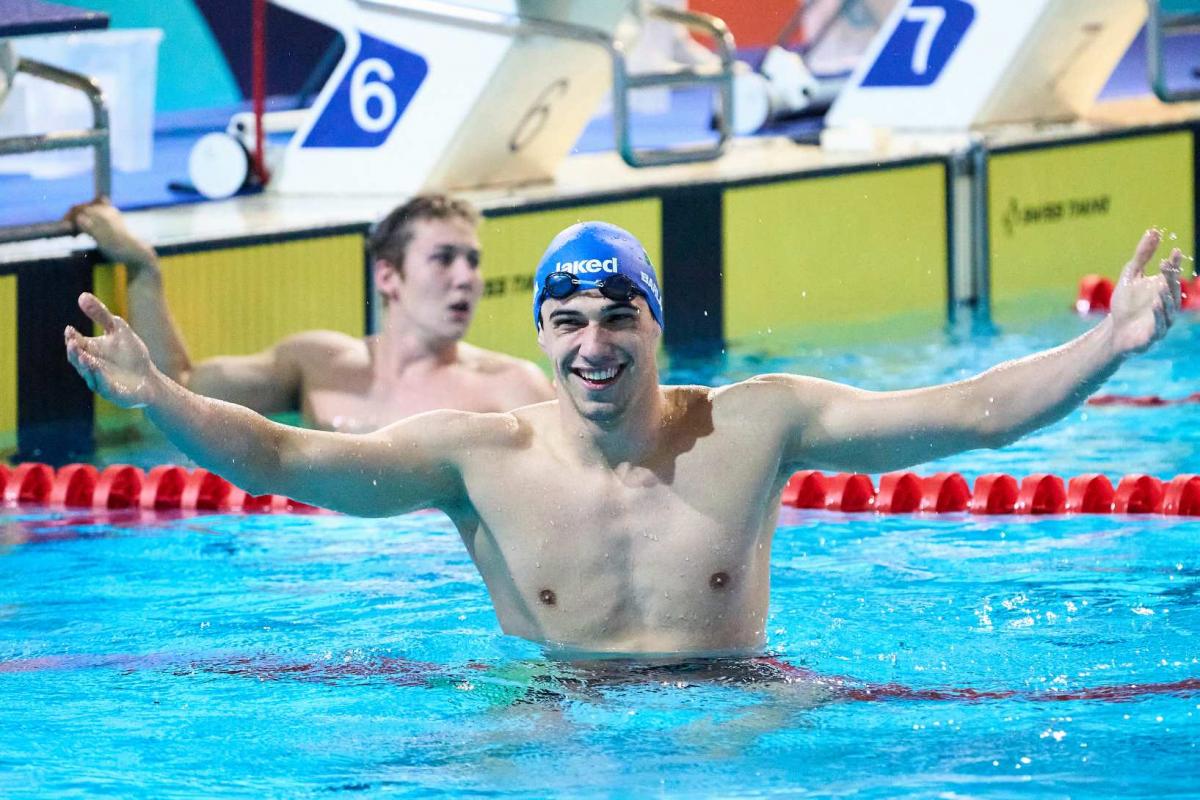 A male swimmer with his arms stretched in a pool with another swimmer in the background