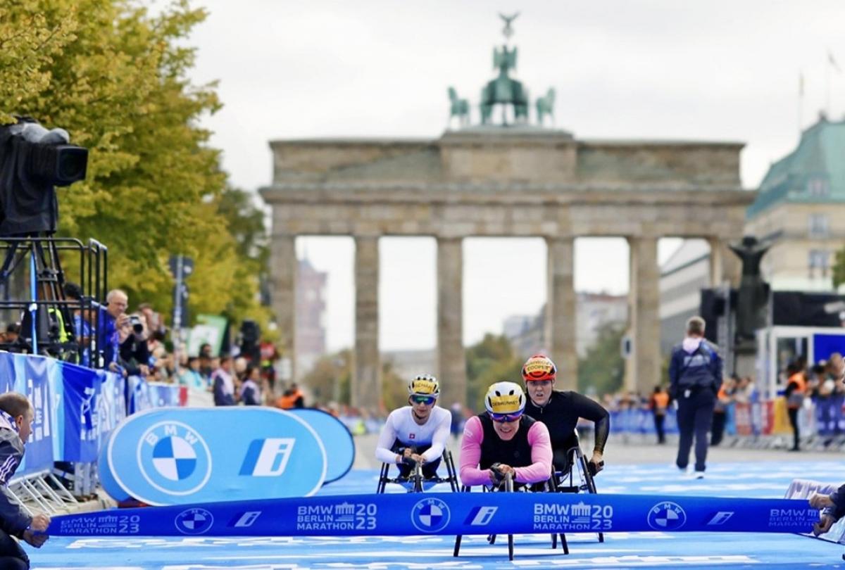 A female wheelchair racer crossing the finishing line of the Berlin Marathon ahead of two competitors