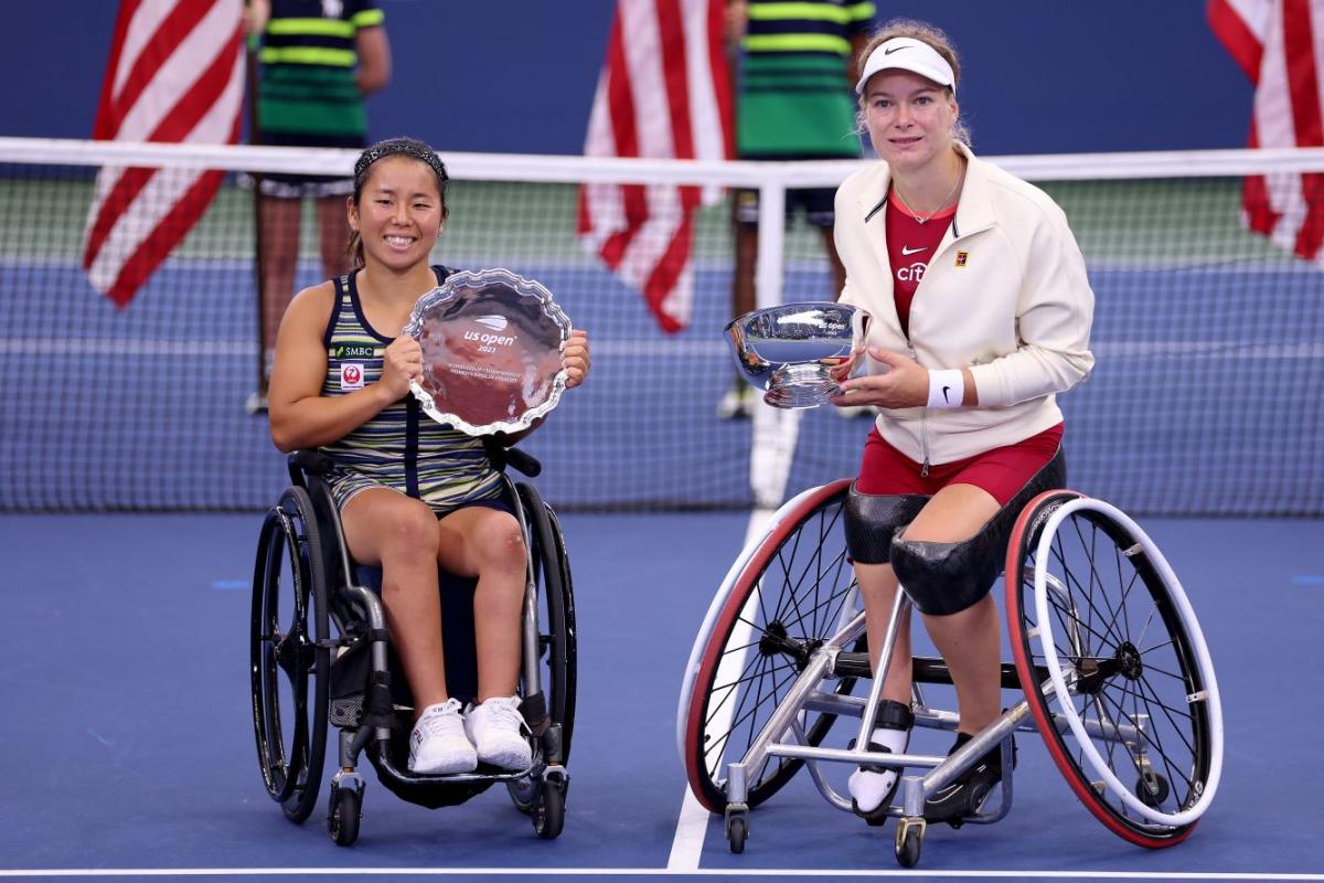 Two female wheelchair tennis athletes pose for a photo on the tennis court with their silverware