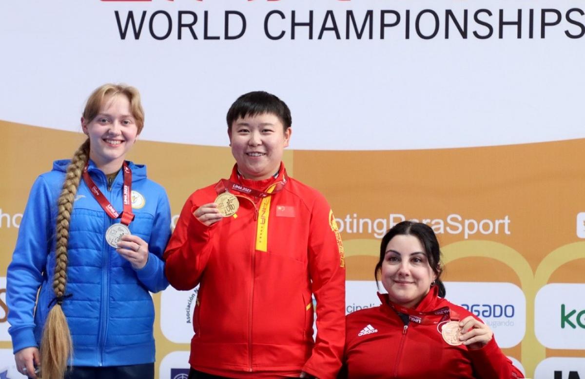 Two women standing next to a seated woman showing their medals