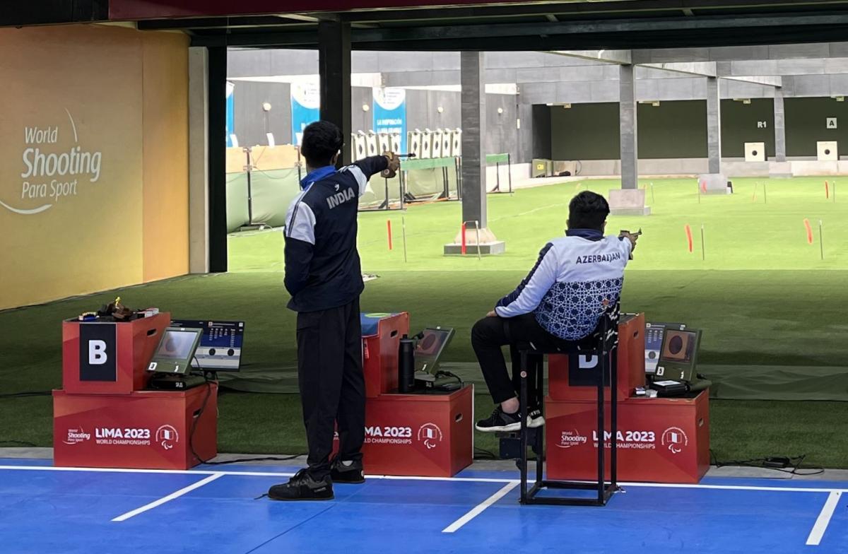 A standing man and a man in a wheelchair competing in a shooting range