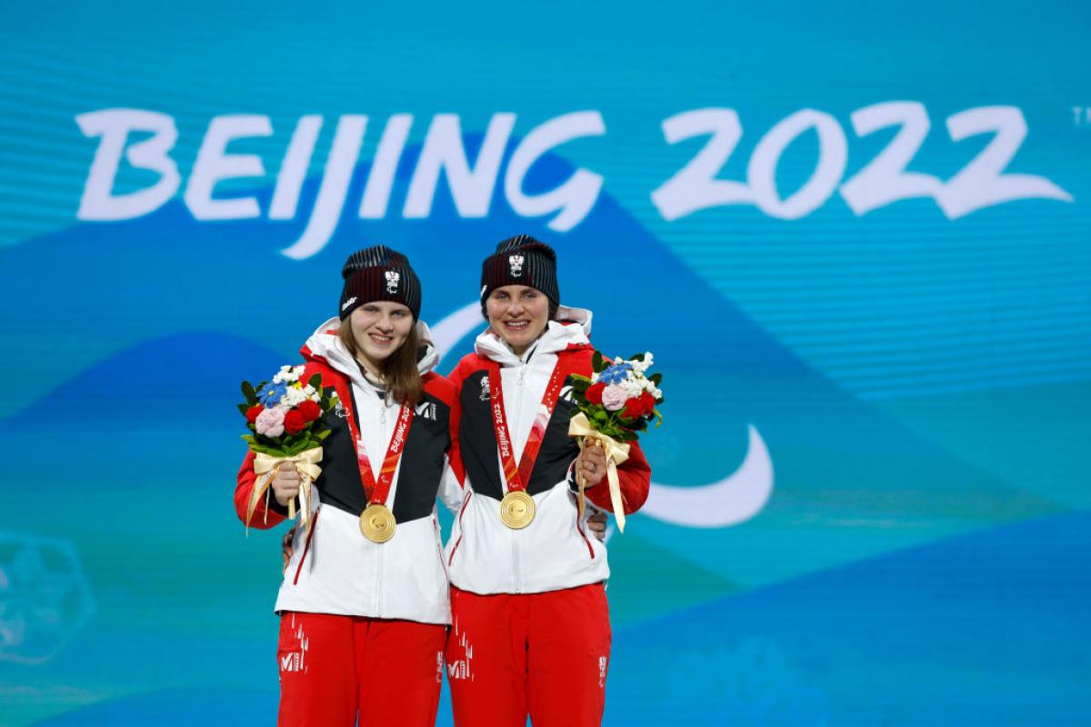 Two female athletes smile for a photograph after receiving gold medals.
