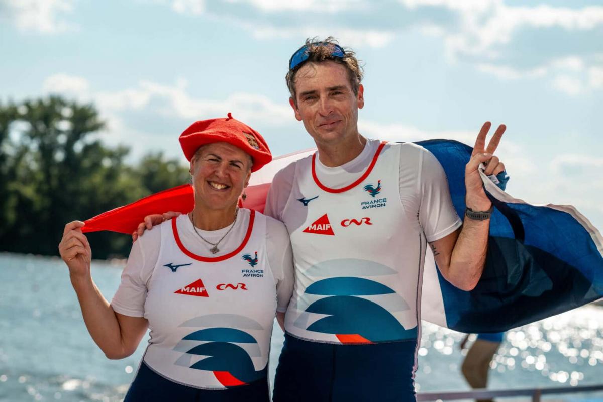 A male and a female Para rower pose for a photograph while holding the French flag.