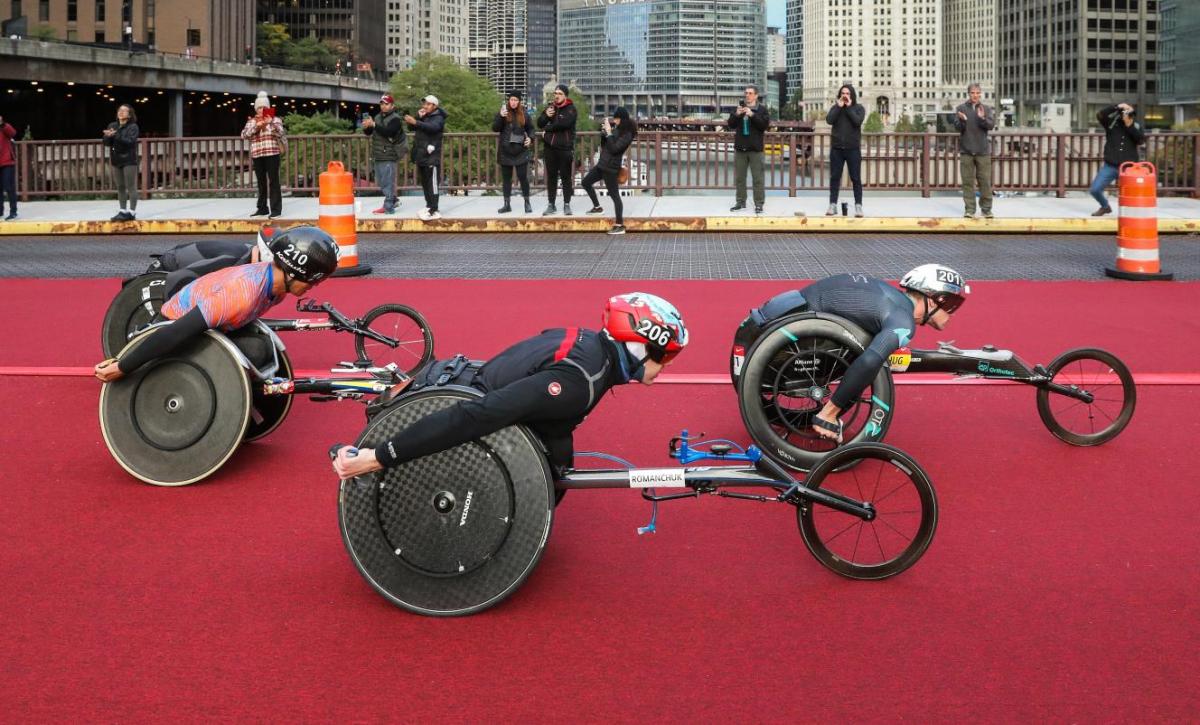 Three male wheelchair racers in a street marathon