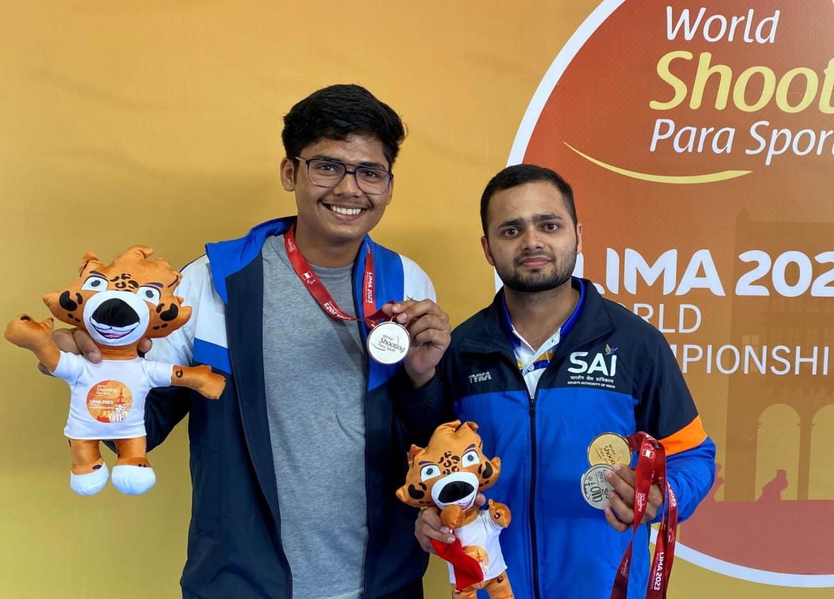 Two athletes holding medals and a mascot plush toy 