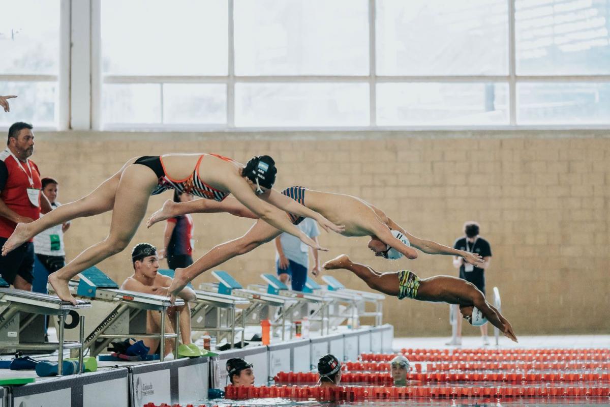 Three Para swimmers jump into the pool