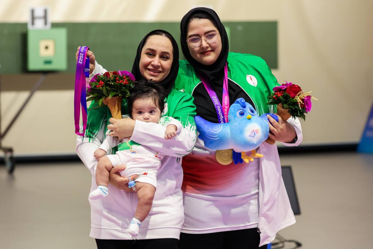 A woman with a headscarf holding a baby next to another woman with a headscarf in a shooting range