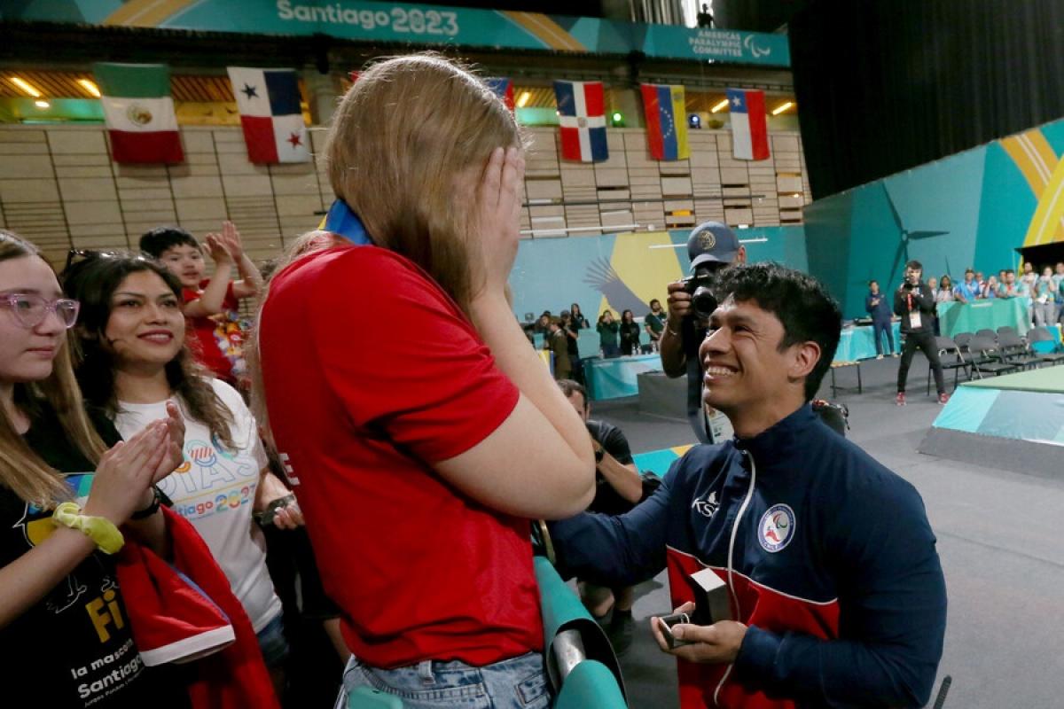 A man in a wheelchair proposing to a standing woman in a competition arena