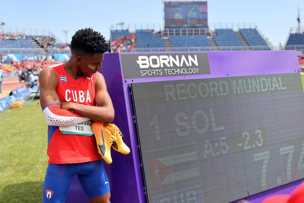 A man standing next to a screen showing his world record on an athletics field