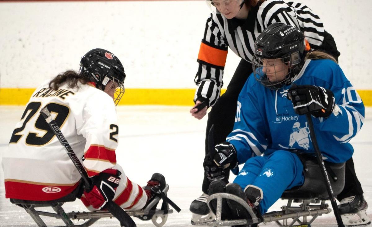 A Para ice hockey official throwing a puck between two female players