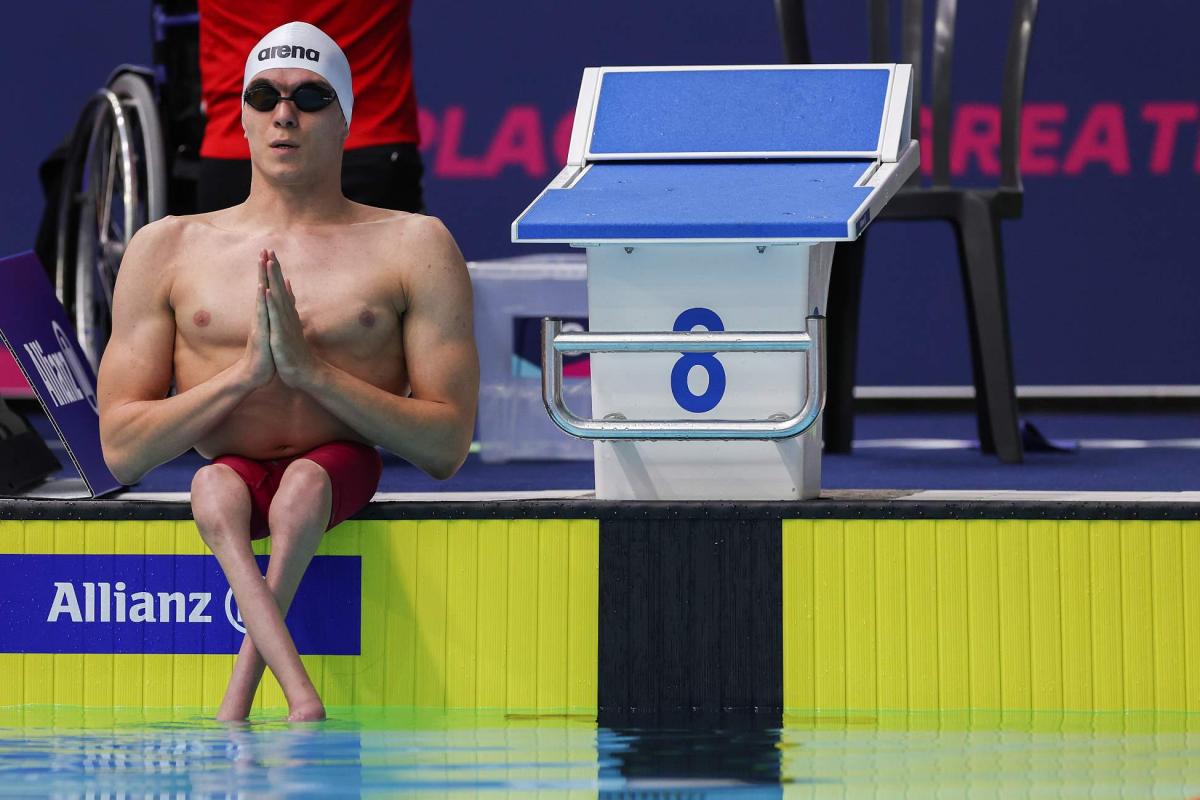 A male Para swimmer seated next to a starting block by a swimming pool