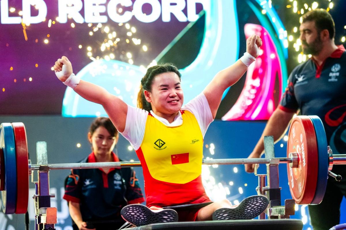 A female athlete on a bench press celebrating with two people in the background