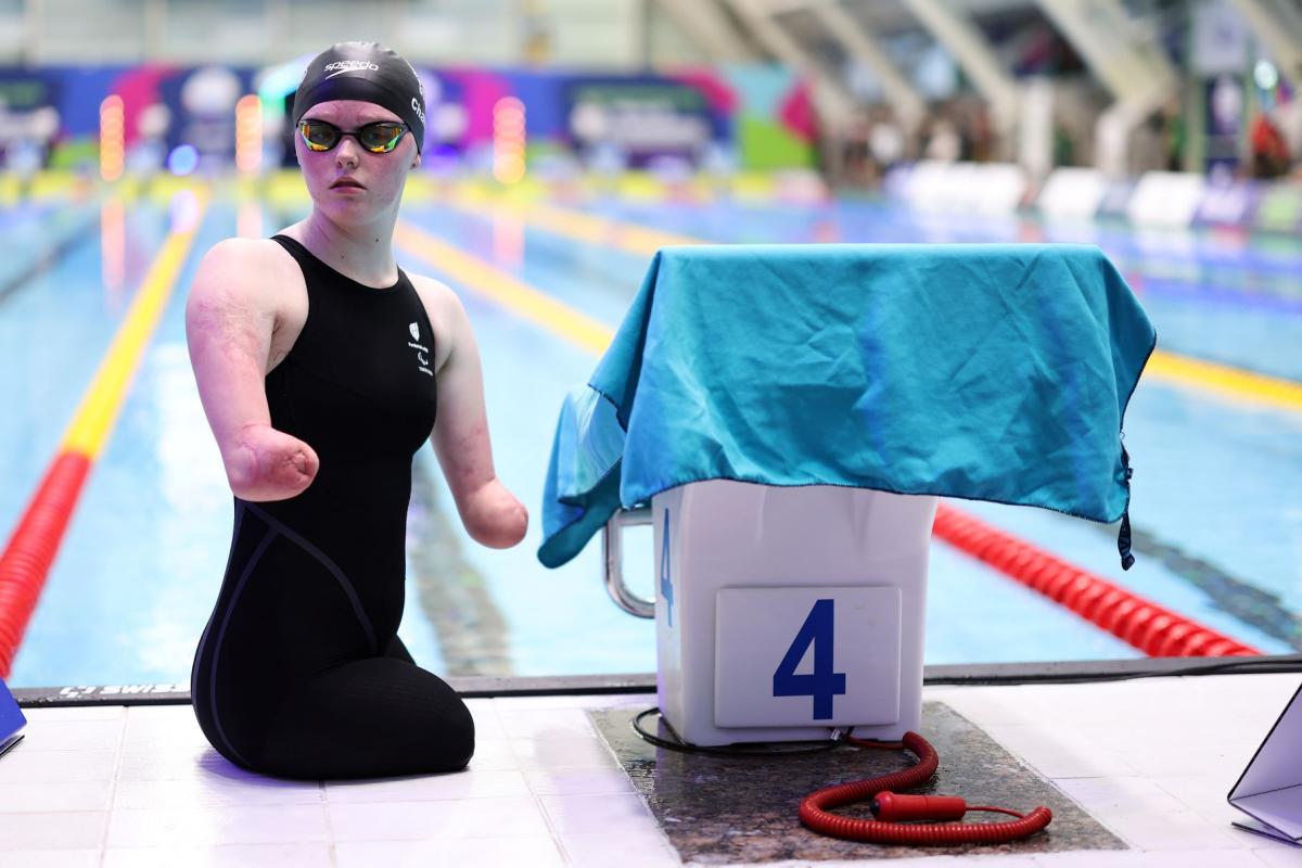 A female Para swimmer next to the starting block of a swimming pool