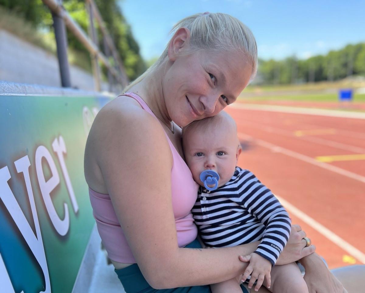 A female athlete sits by the tracks and holds a baby boy.