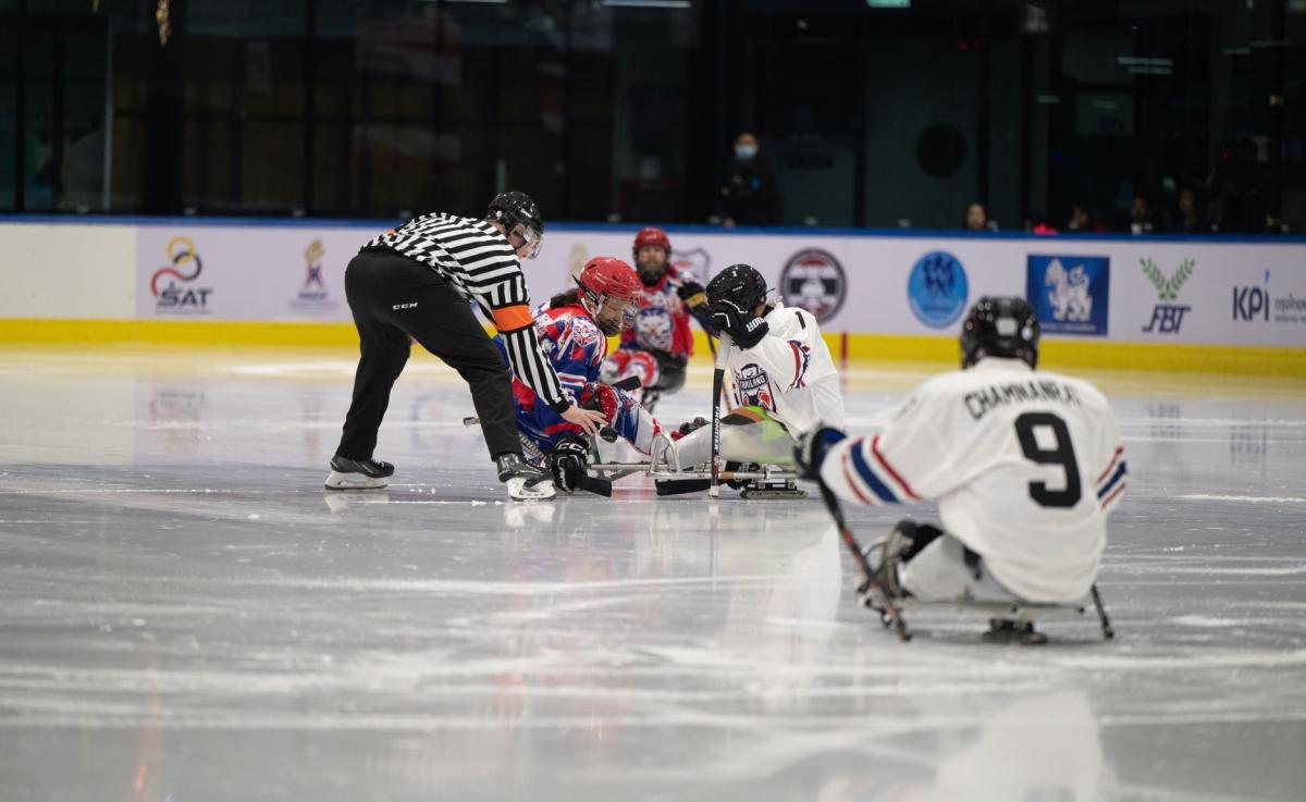 A Para ice hockey referee and two players on a face-off 