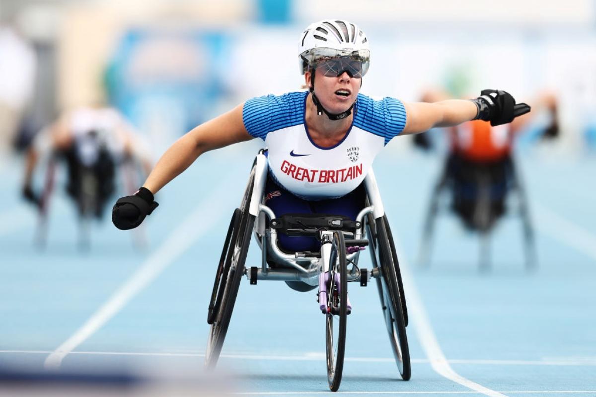 A female wheelchair racer crossing the finish line ahead of two competitors
